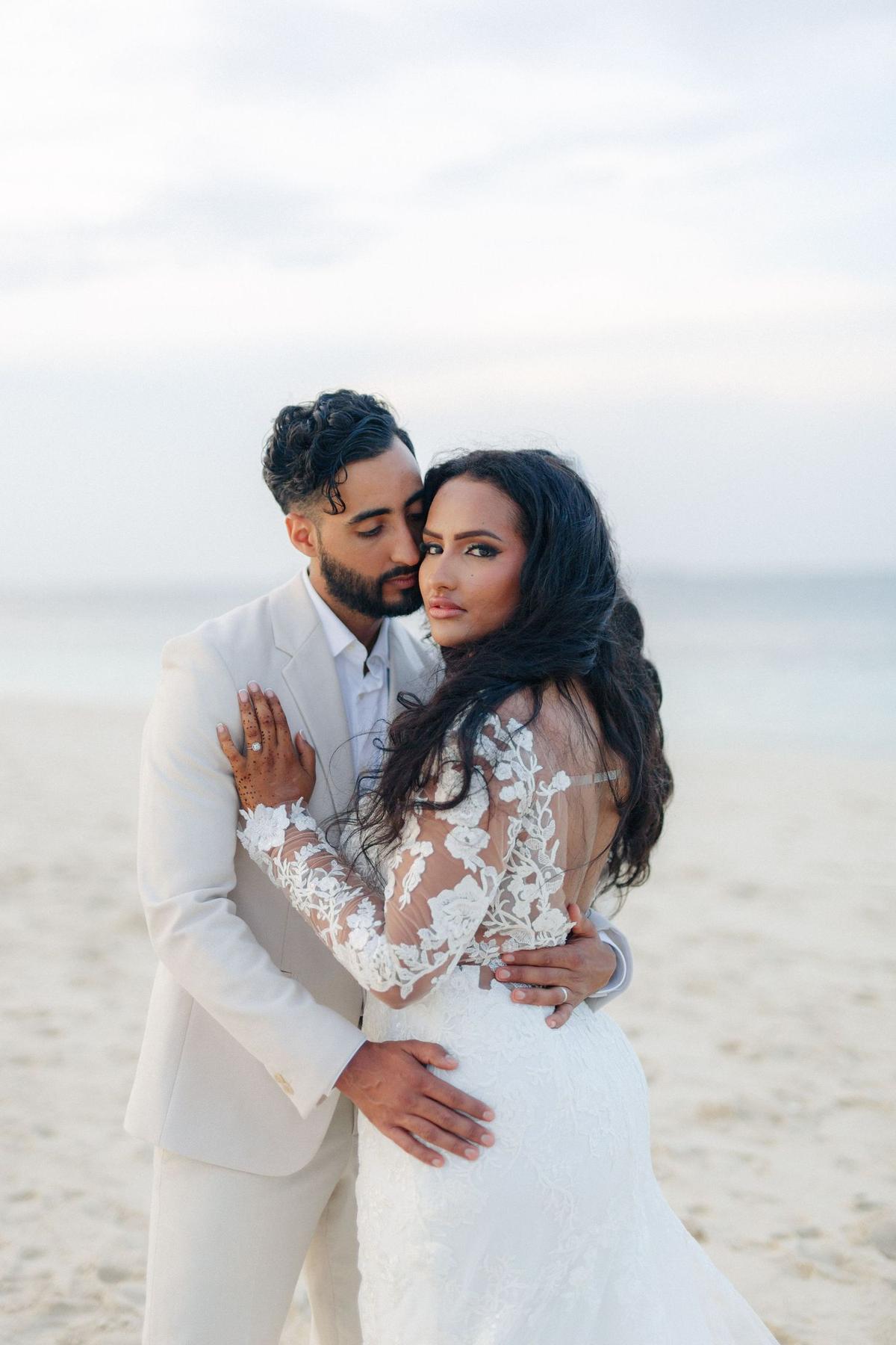 A bride and groom embracing on the beach at dusk
